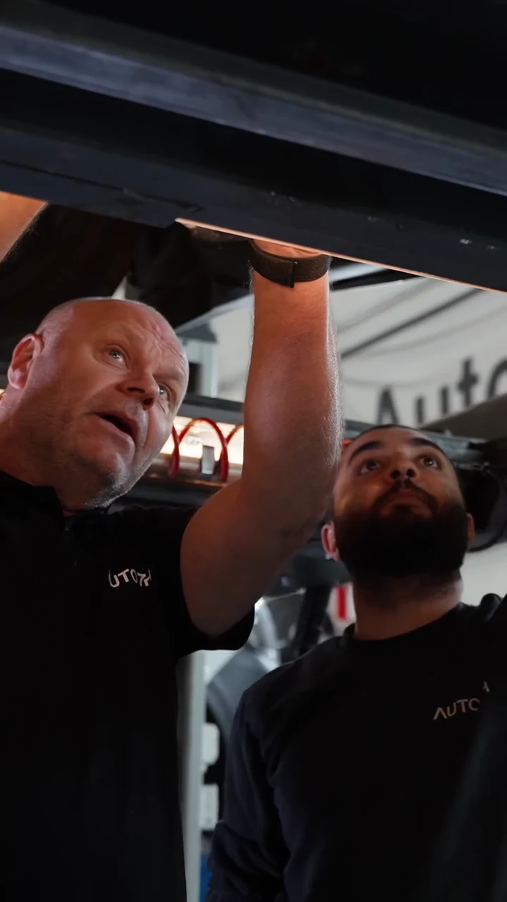 Två medarbetare kontrollerar en upplyft bil hos AUTO7H