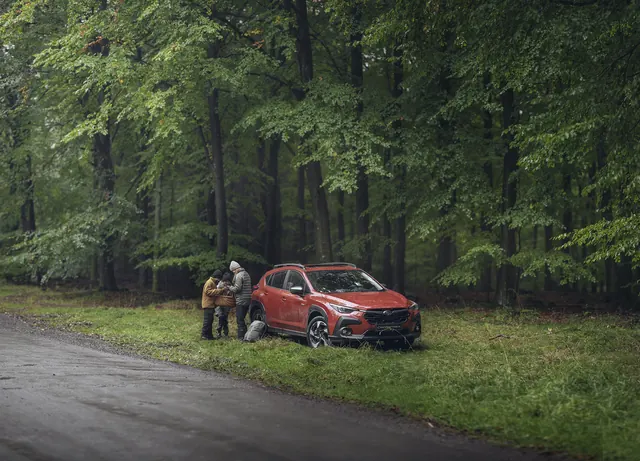 Röd Subaru Crosstrek och en familj vid en skogsväg